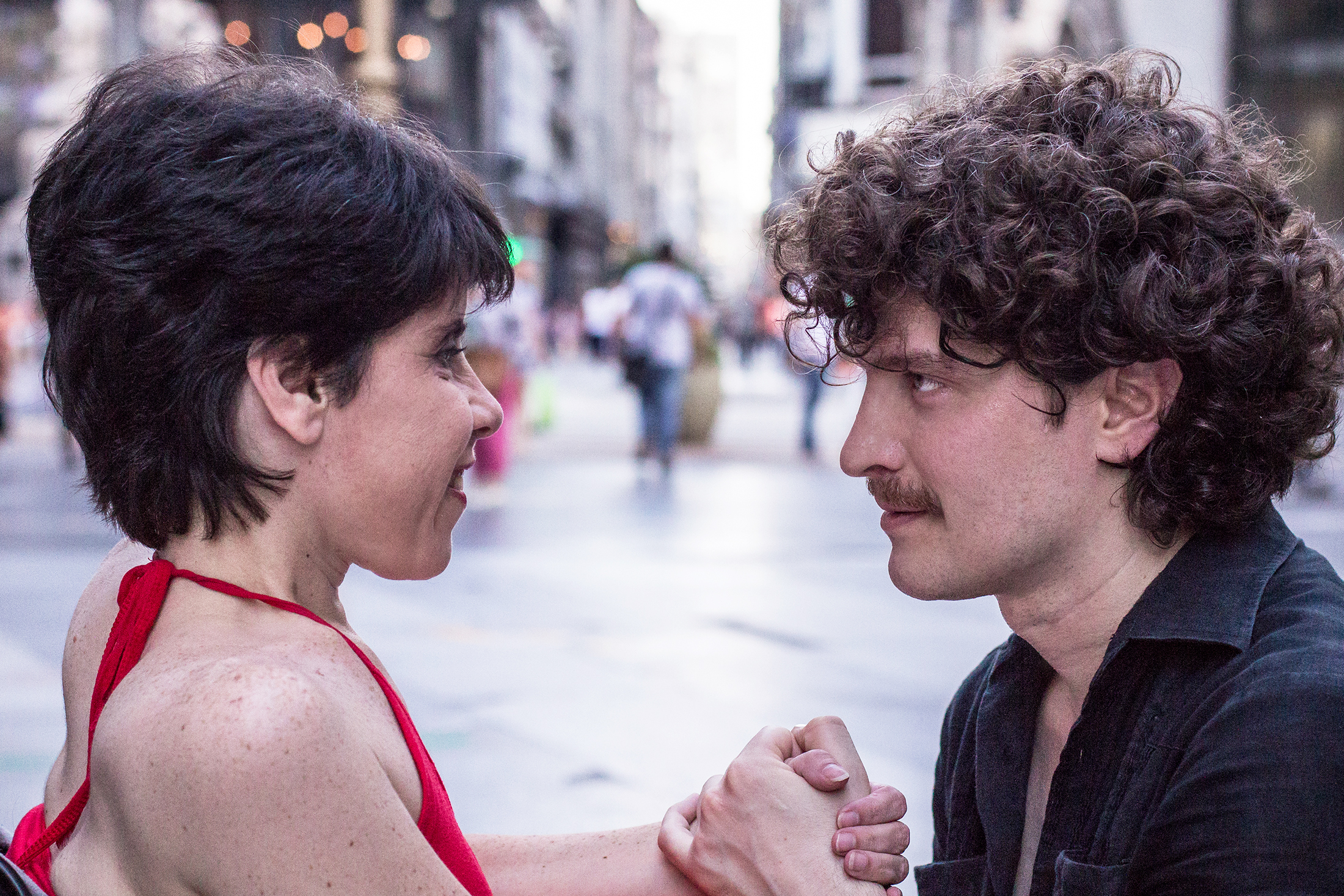 Plano medio de perfil de Brenda y bailarín mirándose fijamente a los ojos sonriendo en la calle Florida en Buenos Aires